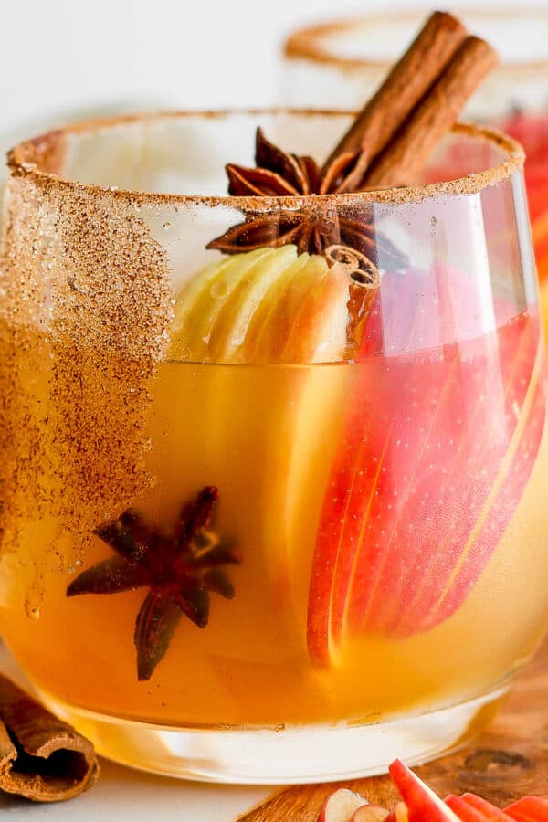 A glass filled with an apple cider margarita with apple slices inside, star anise and a cinnamon stick.