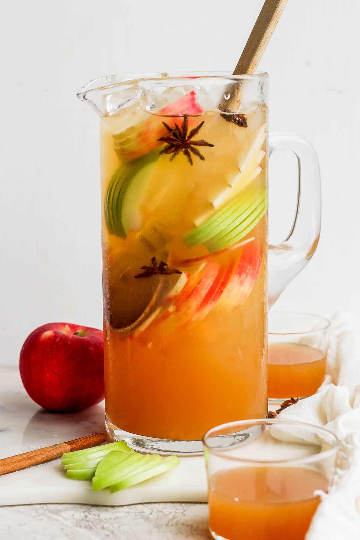 A pitcher of apple cider margarita with apple slices, star anise, and cinnamon sticks.