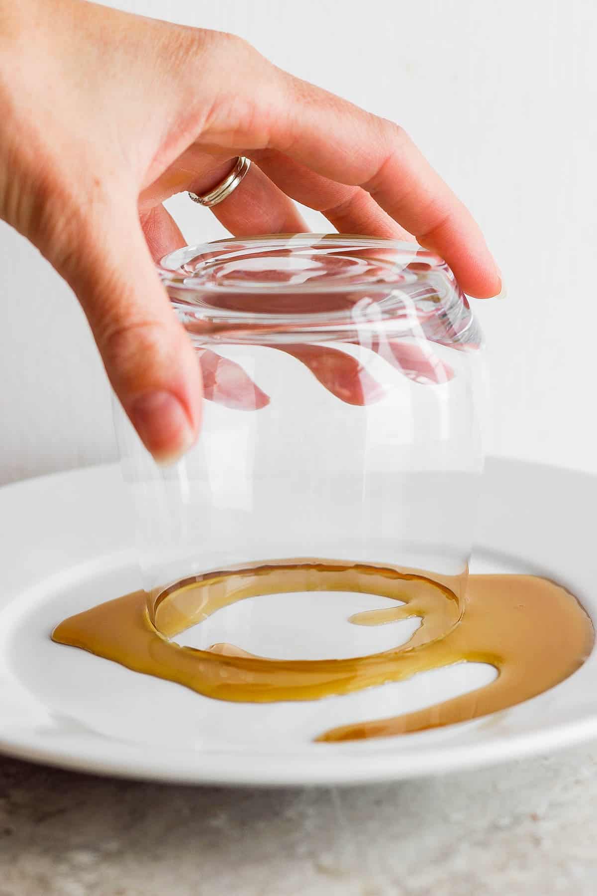 A hand holding a margarita glass upsidown and pressing the rim into a plate of maple syrup.