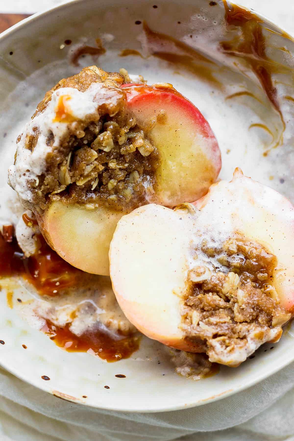 A baked apple cut in half in a bowl with all the toppings.