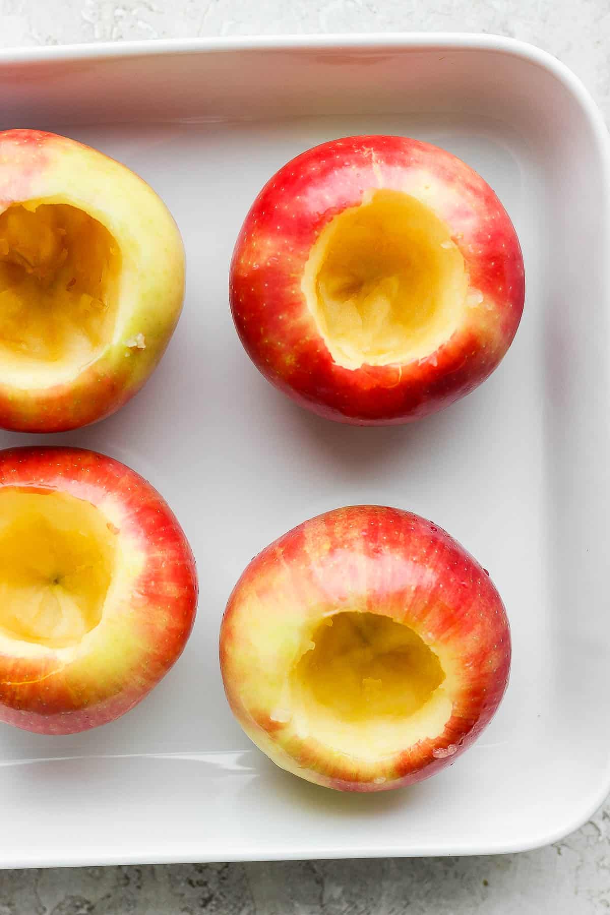 Red apples with the core removed in a white baking dish.