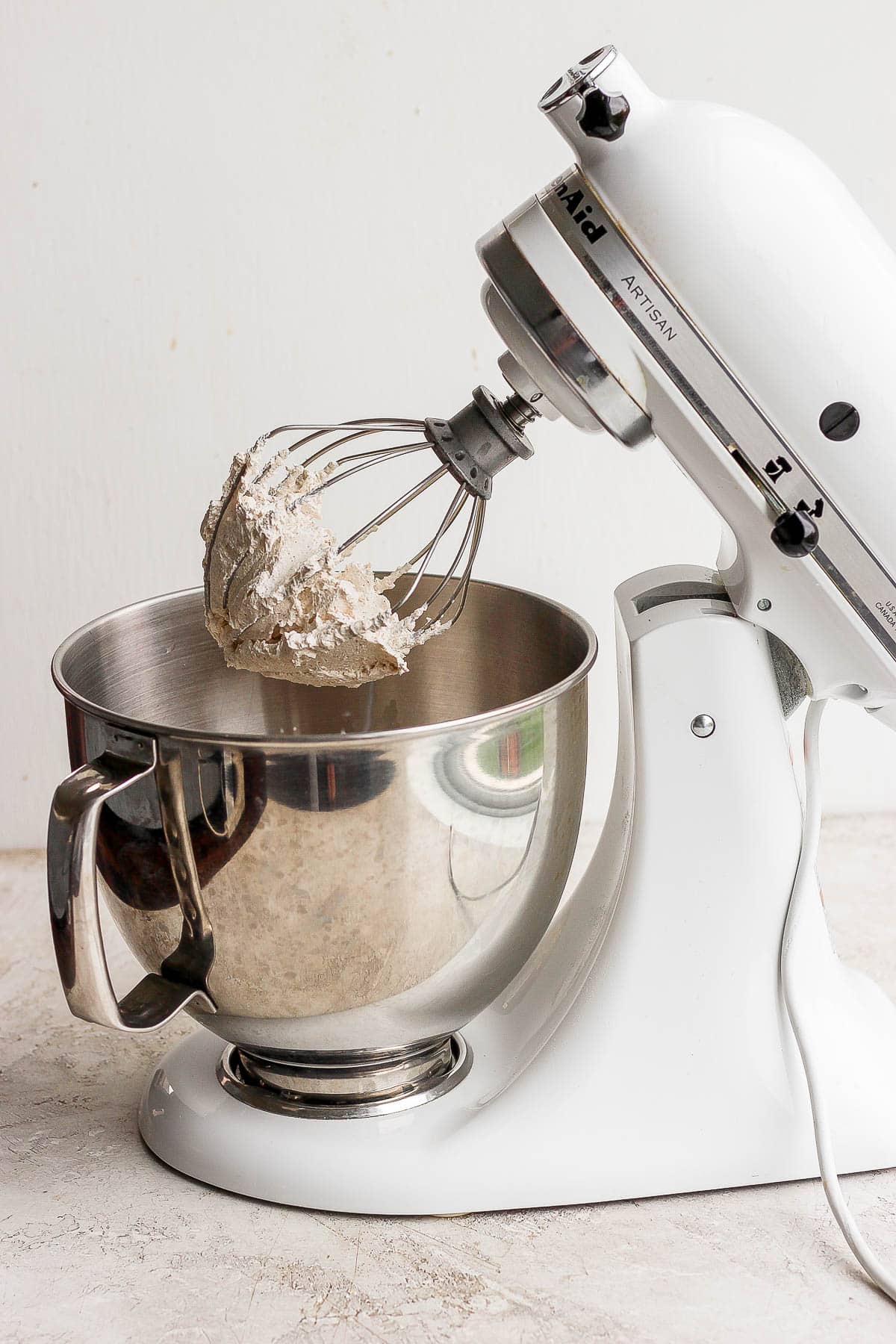 Cardamom whipped cream on a whisk attachment to a stand mixer.