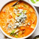 Top down shot of a bowl of buffalo chicken soup garnished with sliced green onion and blue cheese crumbles.