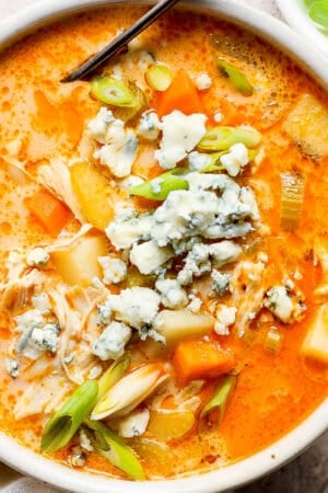 Top down shot of a bowl of buffalo chicken soup garnished with sliced green onion and blue cheese crumbles.