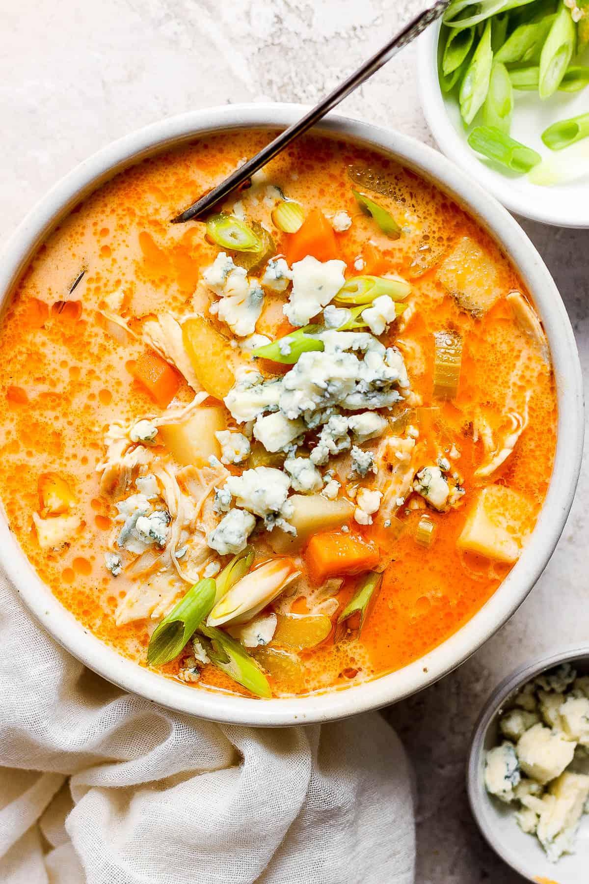 Buffalo chicken soup in a white bowl and topped with green onions and blue cheese.