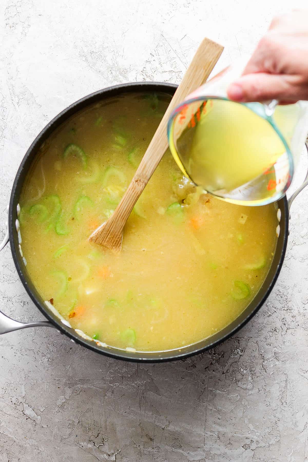 Chicken broth gradually being added to the cooked vegetables in the pot.