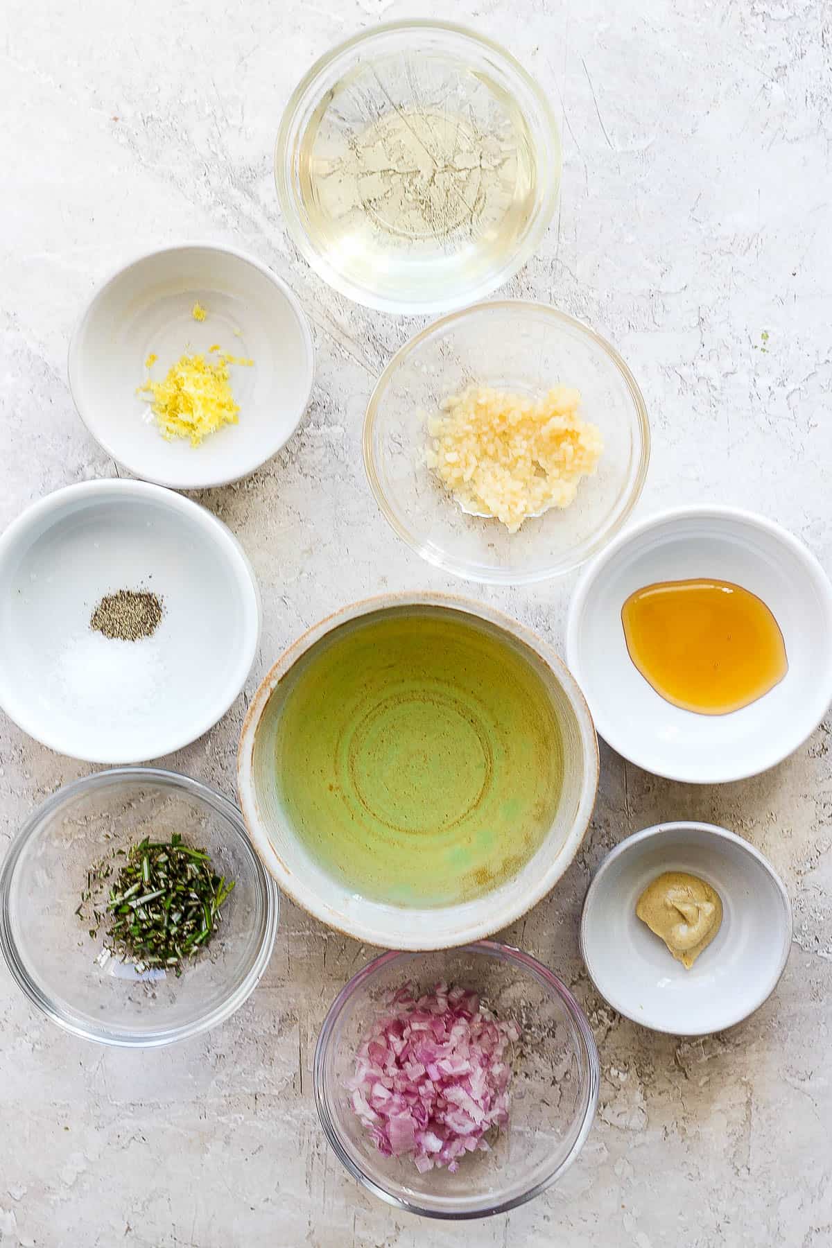 Individual bowls of red onion, dijon mustard, fresh thyme, honey, olive oil, pepper, garlic, lemon zest, and champagne vinegar.
