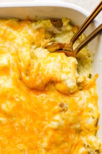 Cheese mashed potatoes in a casserole dish with two spoons.