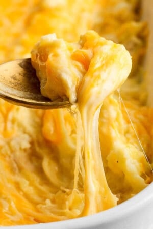 Corner shot of a pan of cheesy mashed potatoes with a spoon lifting out a scoop.