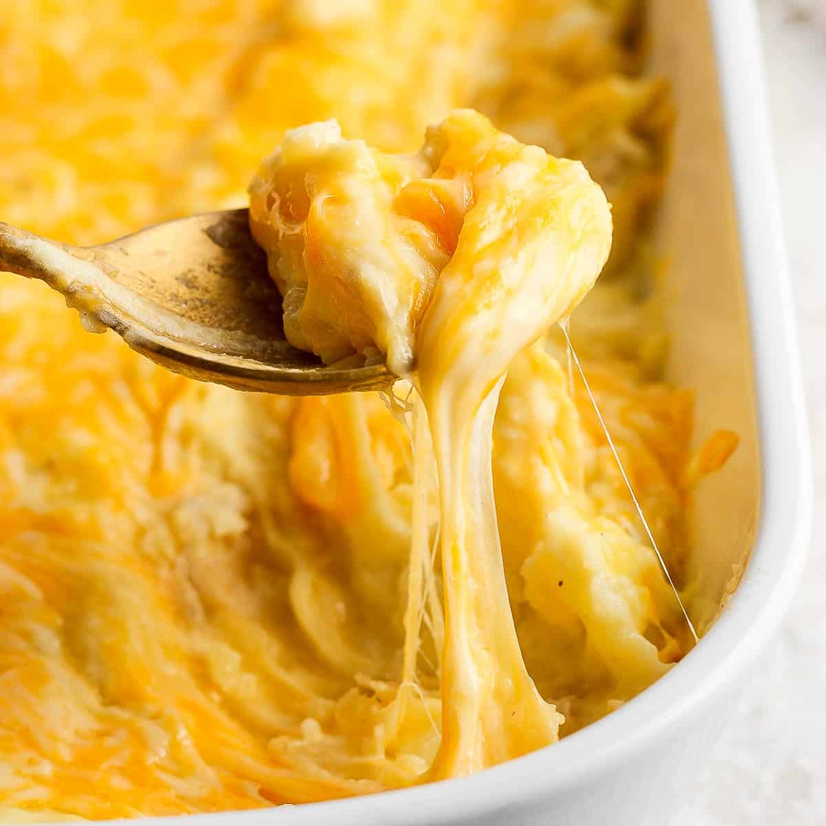 Corner shot of a pan of cheesy mashed potatoes with a spoon lifting out a scoop.