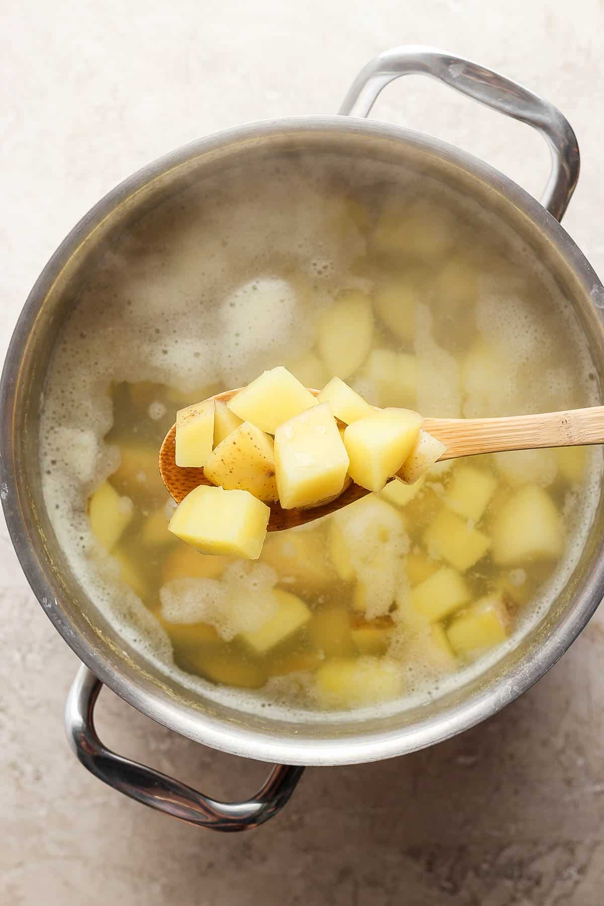 A wooden spoon lifting some cooked potatoes out of a dutch oven.