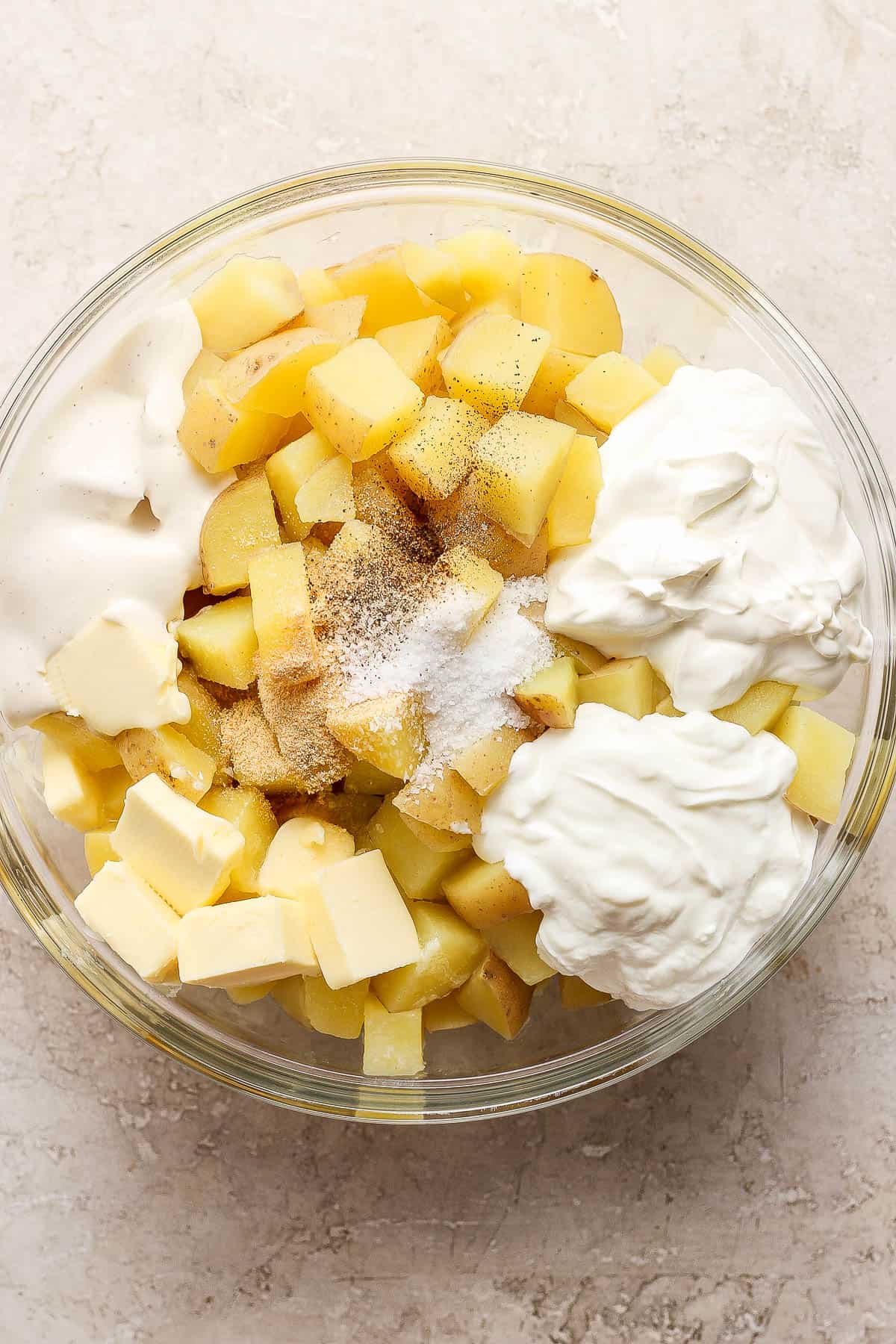 Cooked potatoes placed in a large glass bowl with the rest of the ingredients, except the cheese.