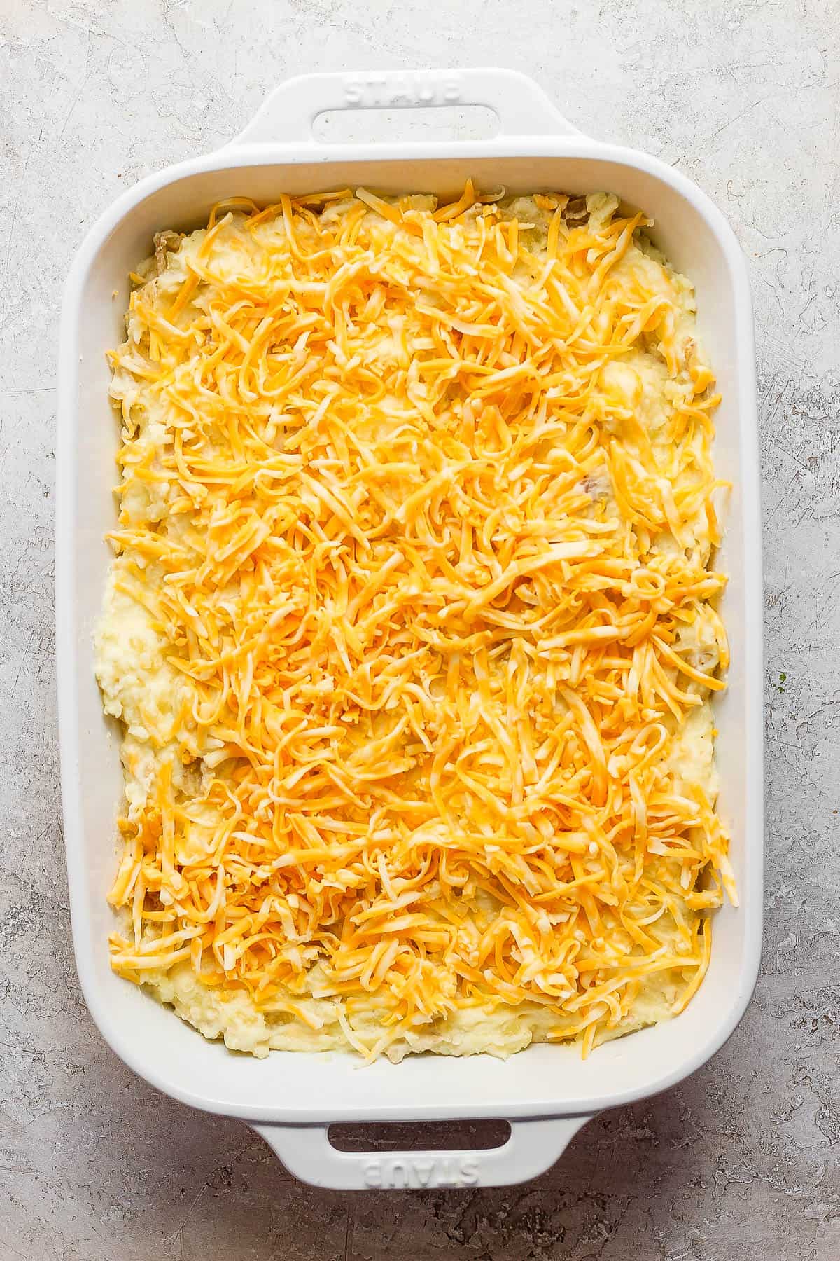 The mashed potatoes added to a white baking dish and the rest of the cheese placed on top.