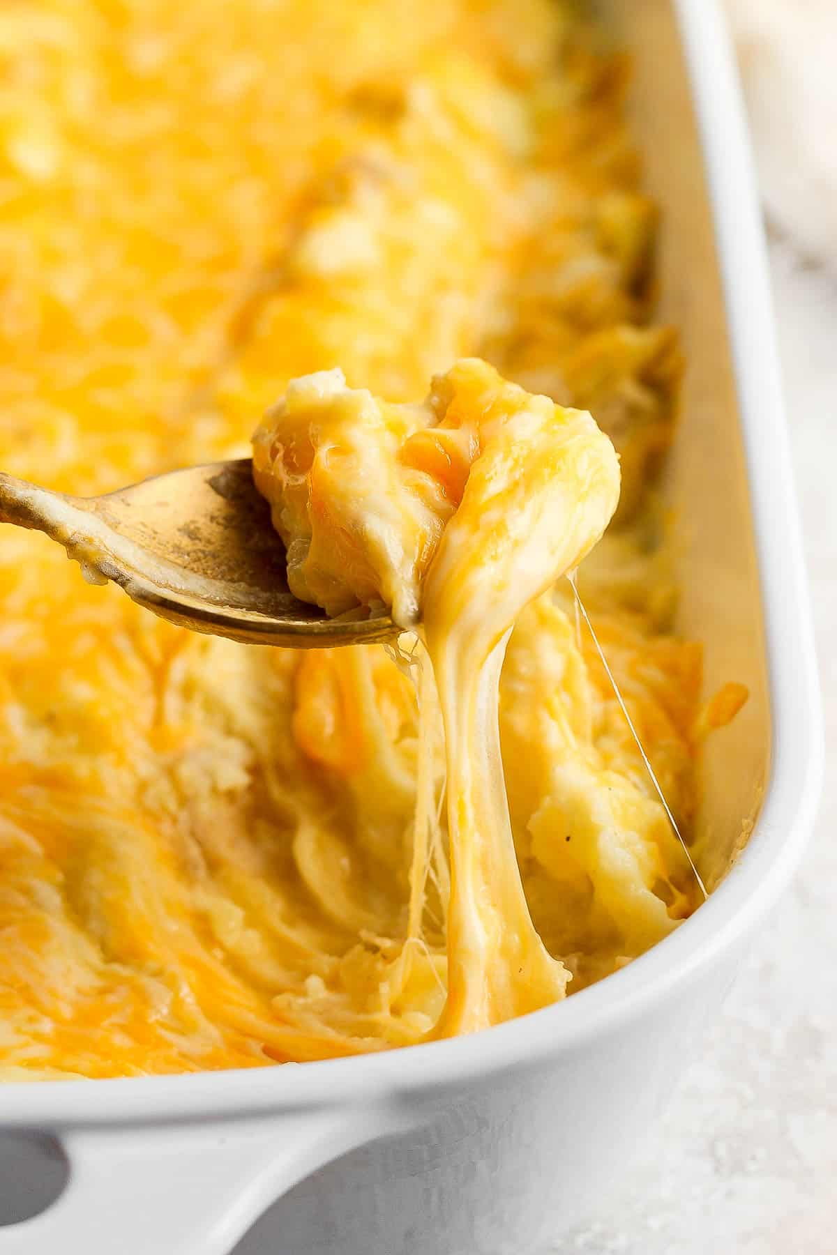 A spoon pulling some of the cheesy mashed potatoes out of the pan.