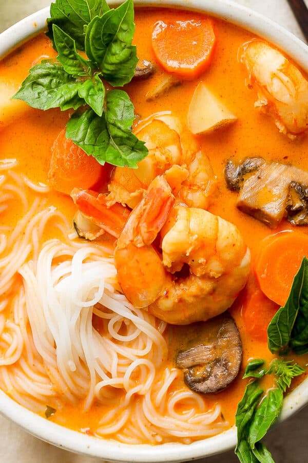 Top down shot of a bowl of coconut curry soup with rice noodles, shrimp and fresh basil leaves.