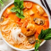 Top down shot of a bowl of coconut curry soup with rice noodles, shrimp and fresh basil leaves.
