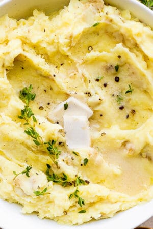 Top down shot of a bowl of dairy free mashed potatoes with fresh thyme and cracked pepper on top.