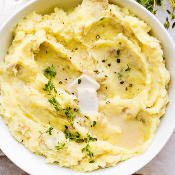 Top down shot of a bowl of dairy free mashed potatoes with fresh thyme and cracked pepper on top.