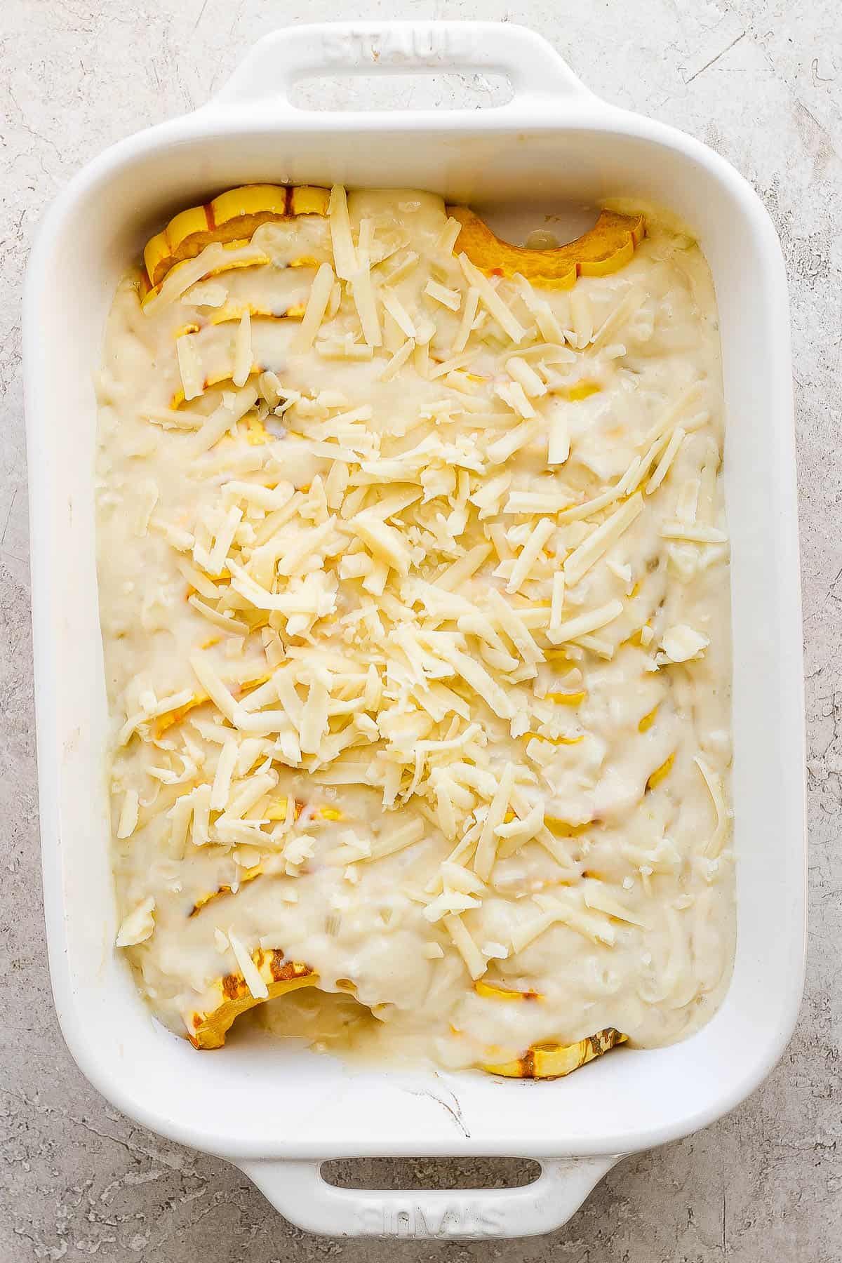 The creamy sauce poured on top of the roasted delicata squash in a baking dish. The rest of the gruyere cheese is sprinkled on top.