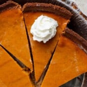 Slices of pumpkin pie in an aluminum tin with a dollop of whipped cream on top of one slice.
