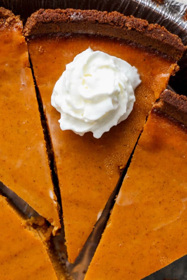 Slices of pumpkin pie in an aluminum tin with a dollop of whipped cream on top of one slice.