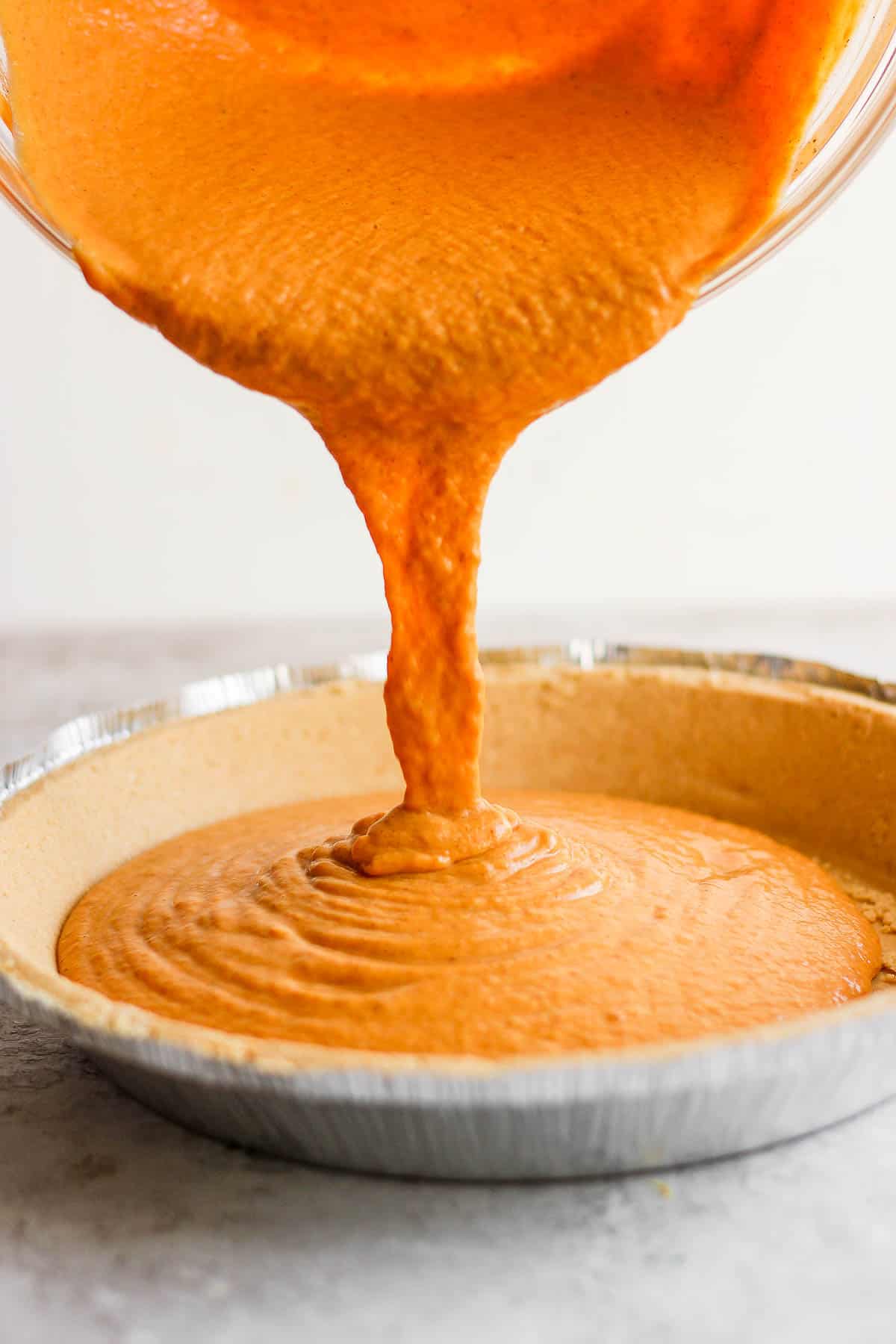 Pumpkin pie filling being poured into a store bought pie crust.