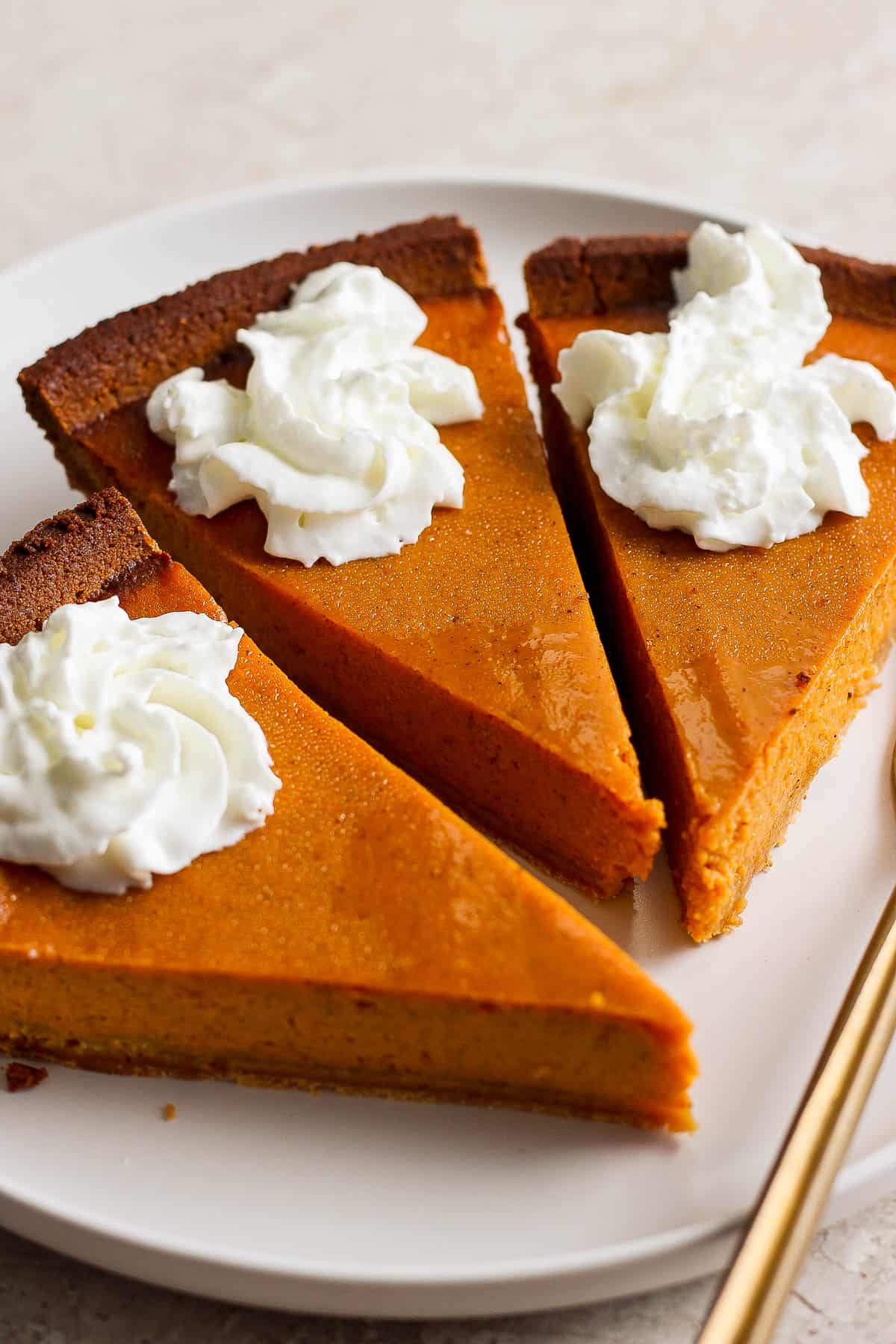 Three slices of pumpkin pie with whipped cream on a white plate.