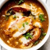Top down shot of a bowl of french onion soup with melted gruyere cheese on top of toasted baguettes with fresh chopped parsley.