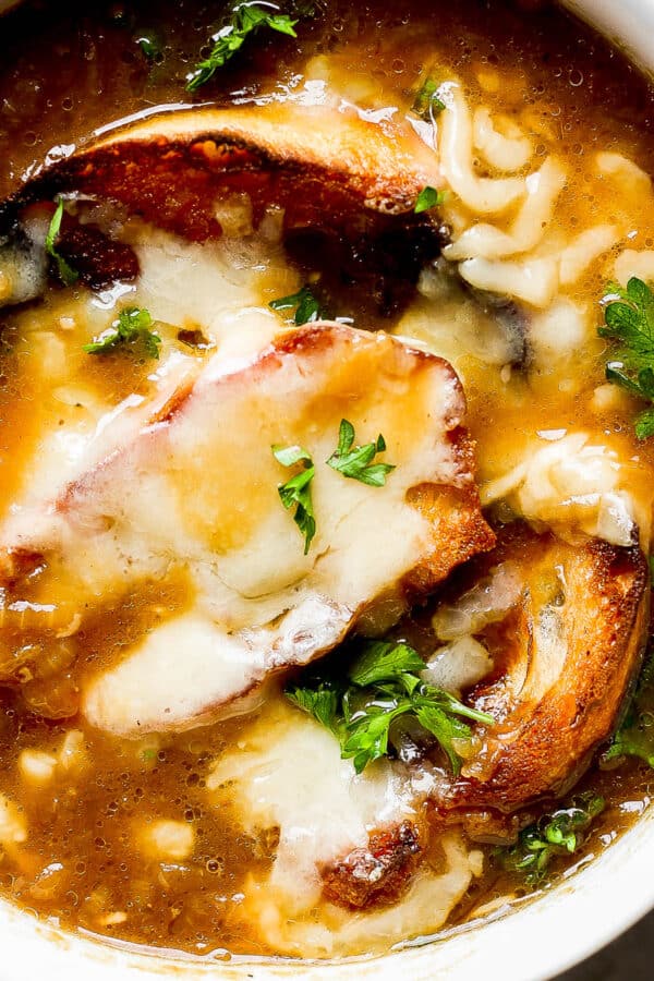 Top down shot of a bowl of french onion soup with melted gruyere cheese on top of toasted baguettes with fresh chopped parsley.