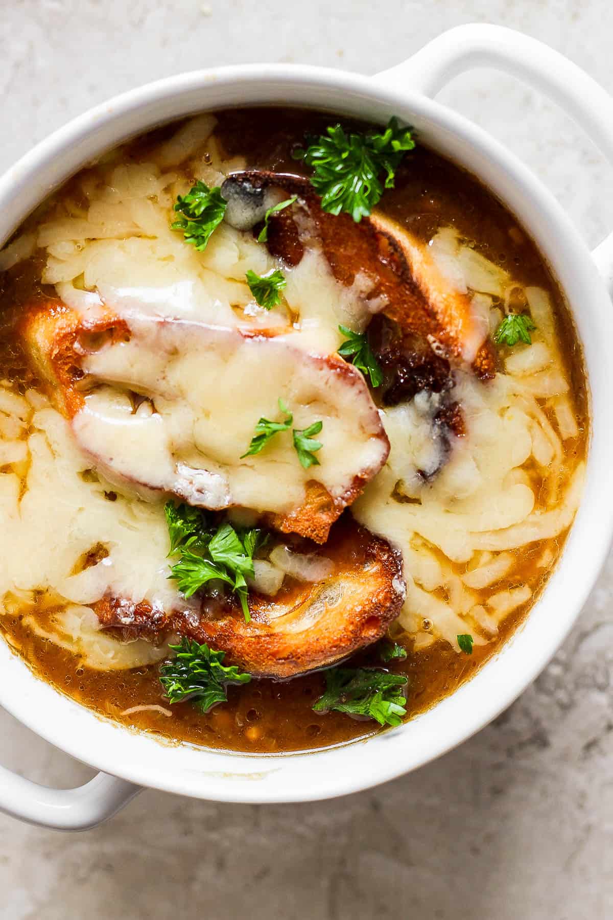 French onion soup in a bowl topped with crusty bread and cheese.