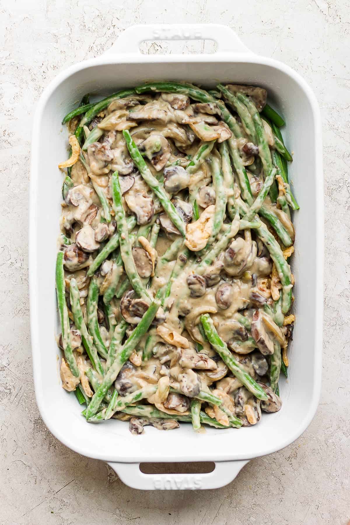 The entire green bean casserole fully mixed and ready to bake in a white casserole dish.