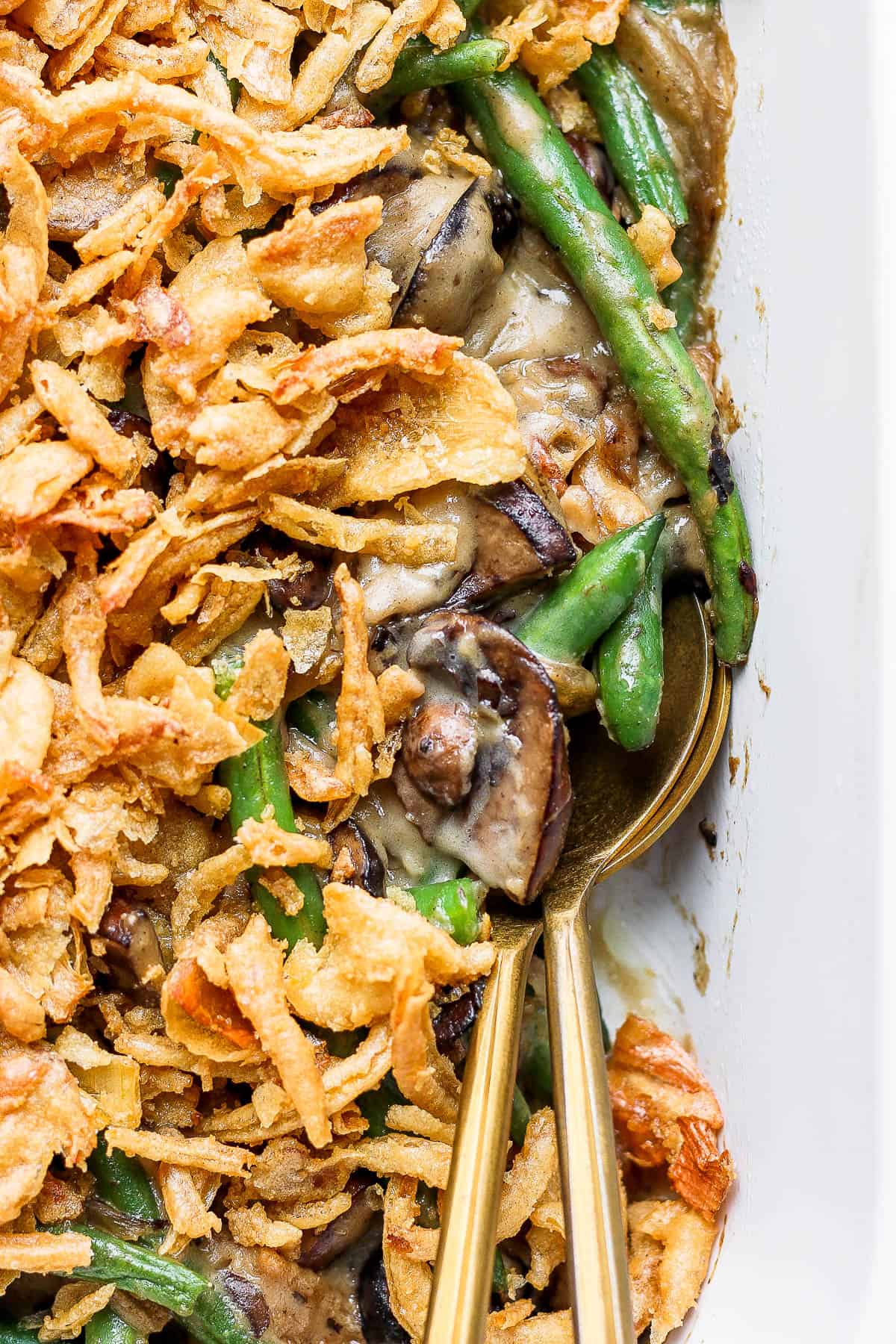 A fully cooked gluten free green bean casserole with two spoons in it.