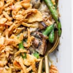 Top down shot of two spoons sticking out of a pan of gluten free green bean casserole with french fried onions on top.