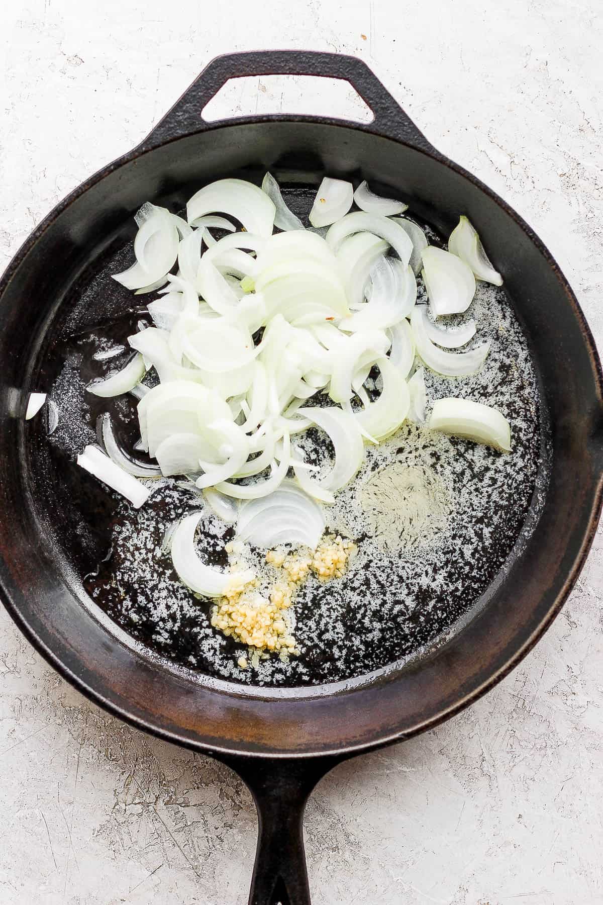 A large skillet with melted butter, garlic, and onion.