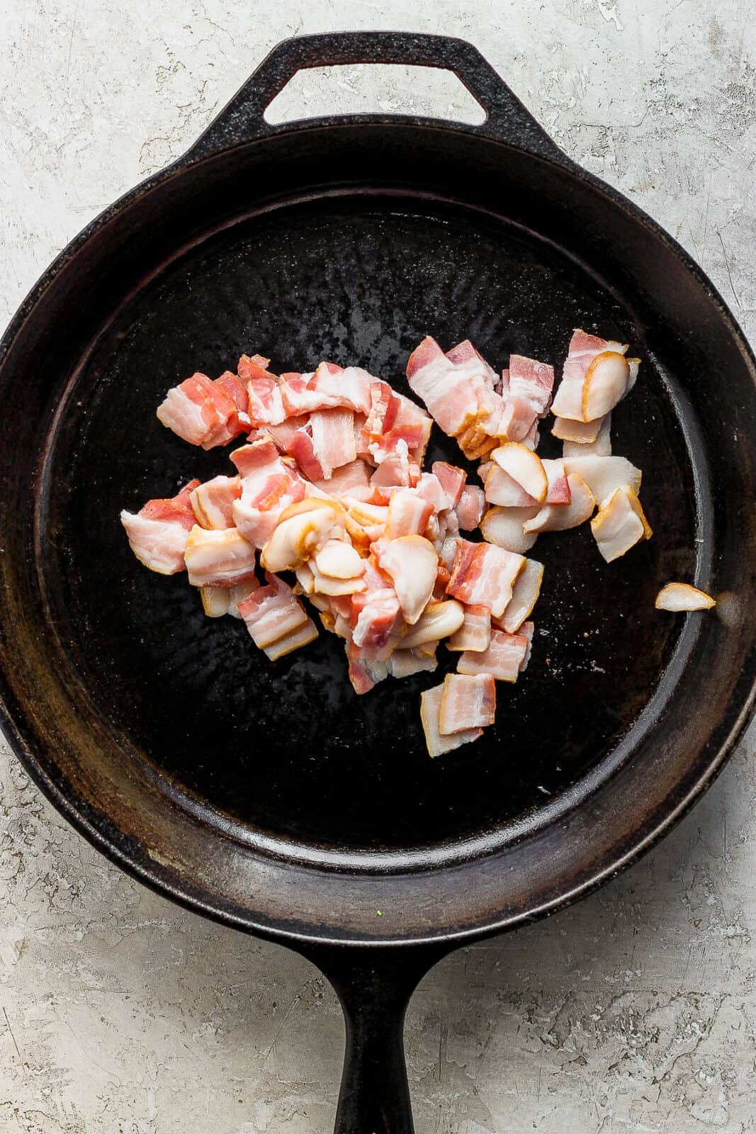 Thick cut bacon cut into bite sized pieces in a cast iron skillet to make green beans with bacon.