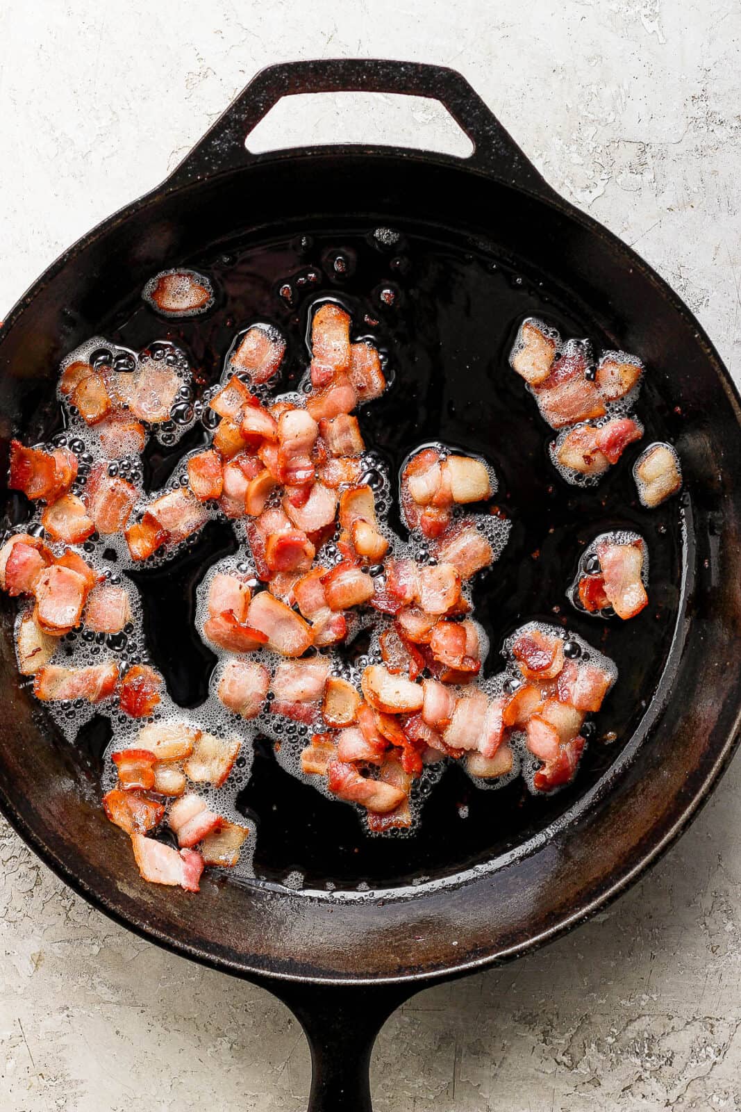 Bite sized pieces of cooked bacon in a cast iron skillet to make green beans with bacon.