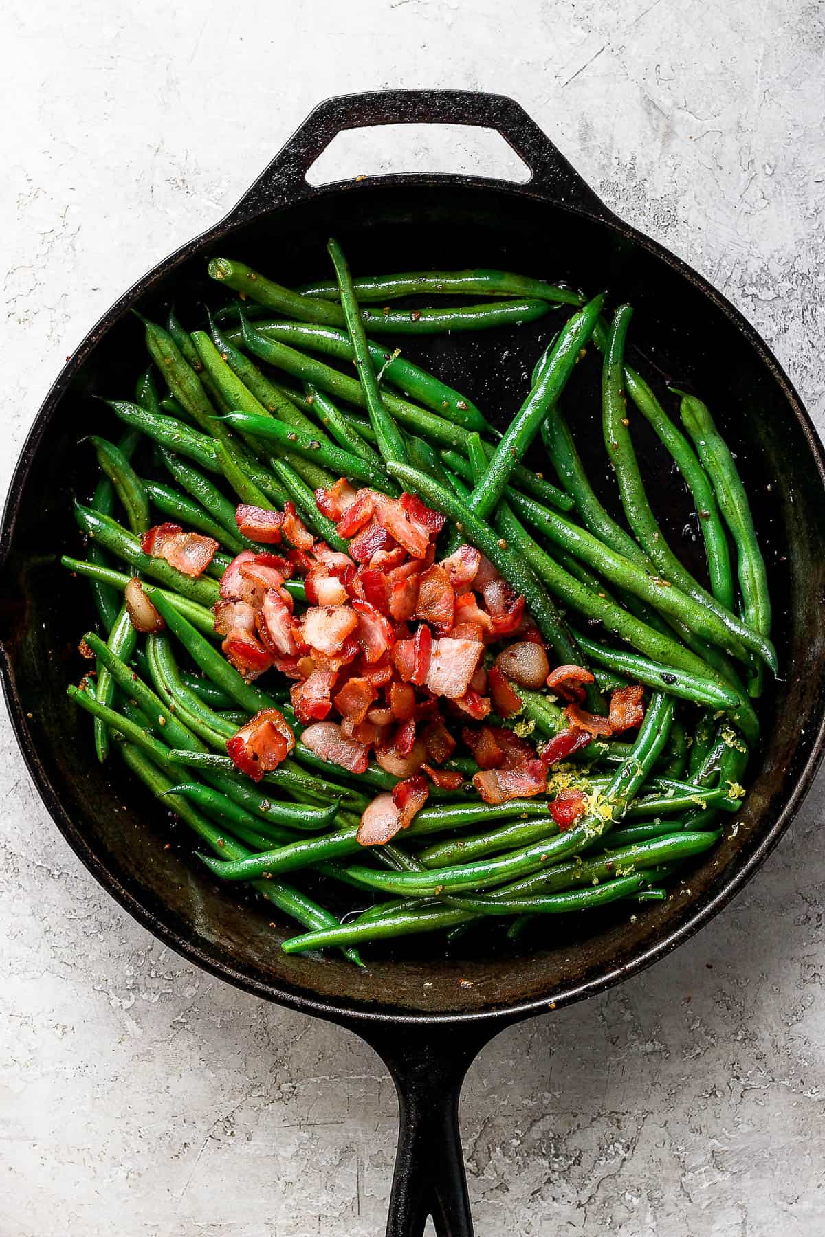 Cooked bacon on top of the green beans in the cast iron skillet.