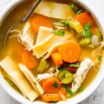 Top down shot of a bowl of homemade chicken noodle soup with homemade noodles and a spoon sticking out.