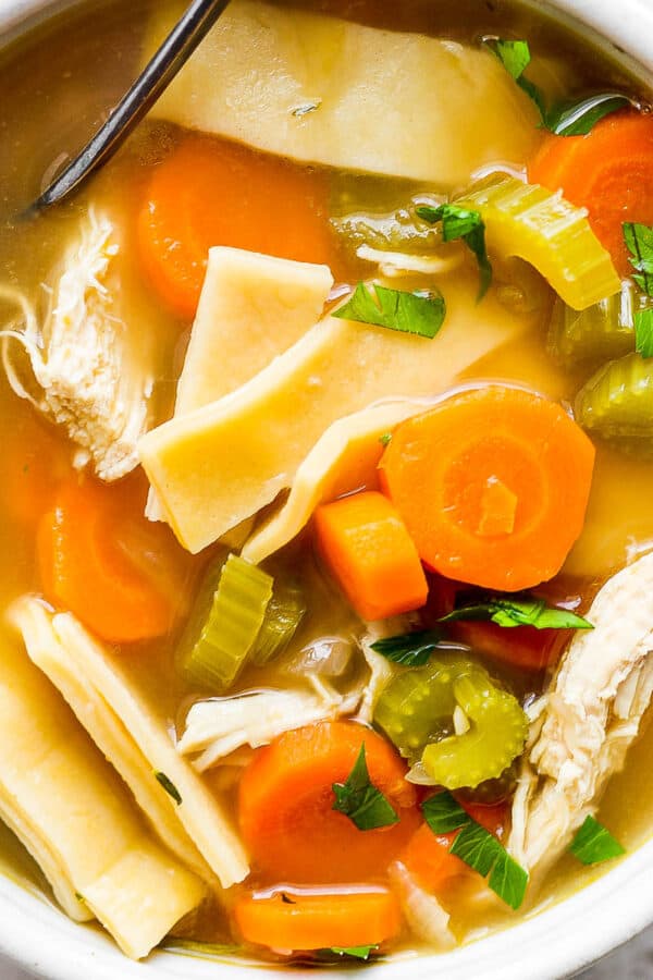 Top down shot of a bowl of homemade chicken noodle soup with homemade noodles and a spoon sticking out.