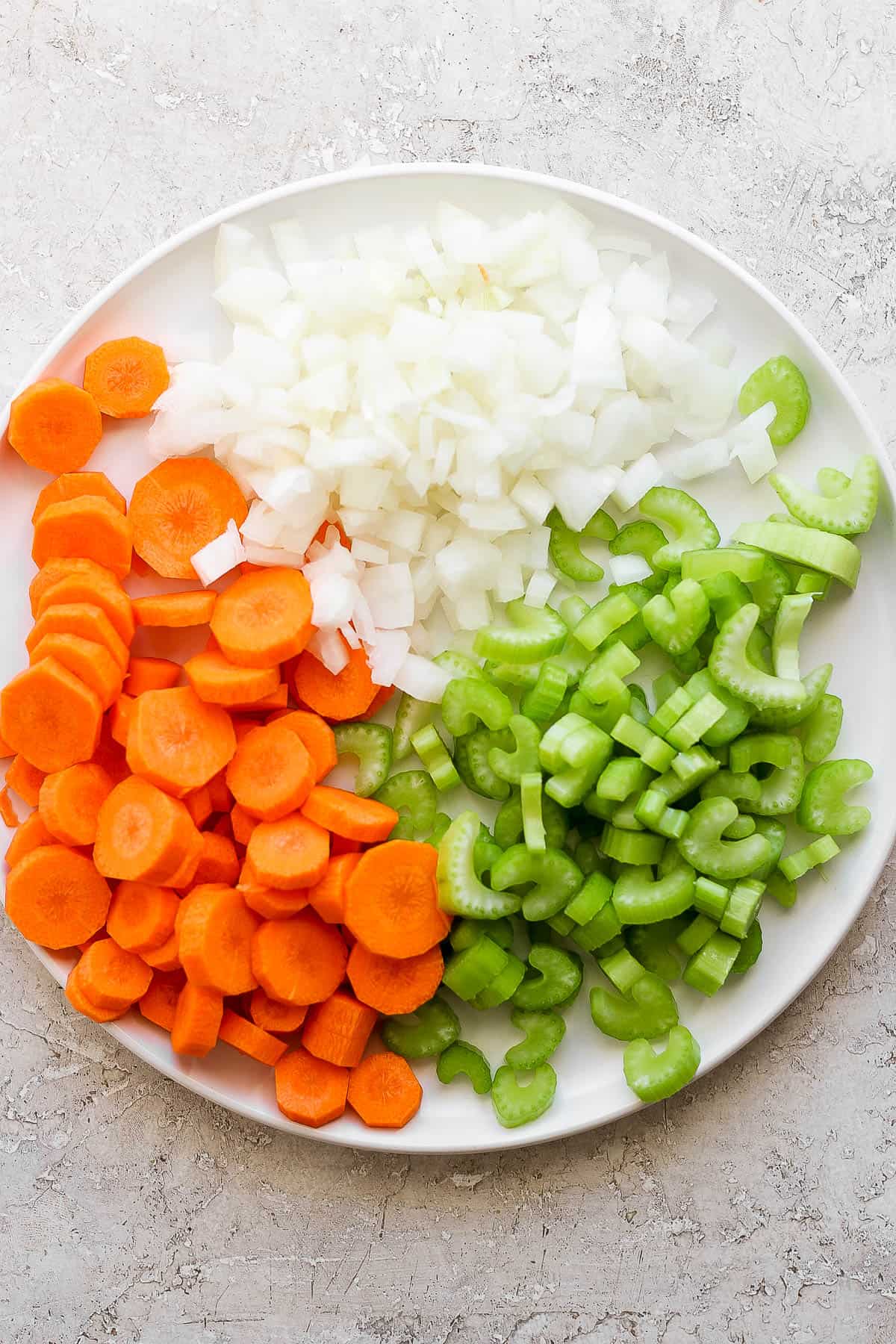 Fresh veggies and onion, chopped and on a large white plate.