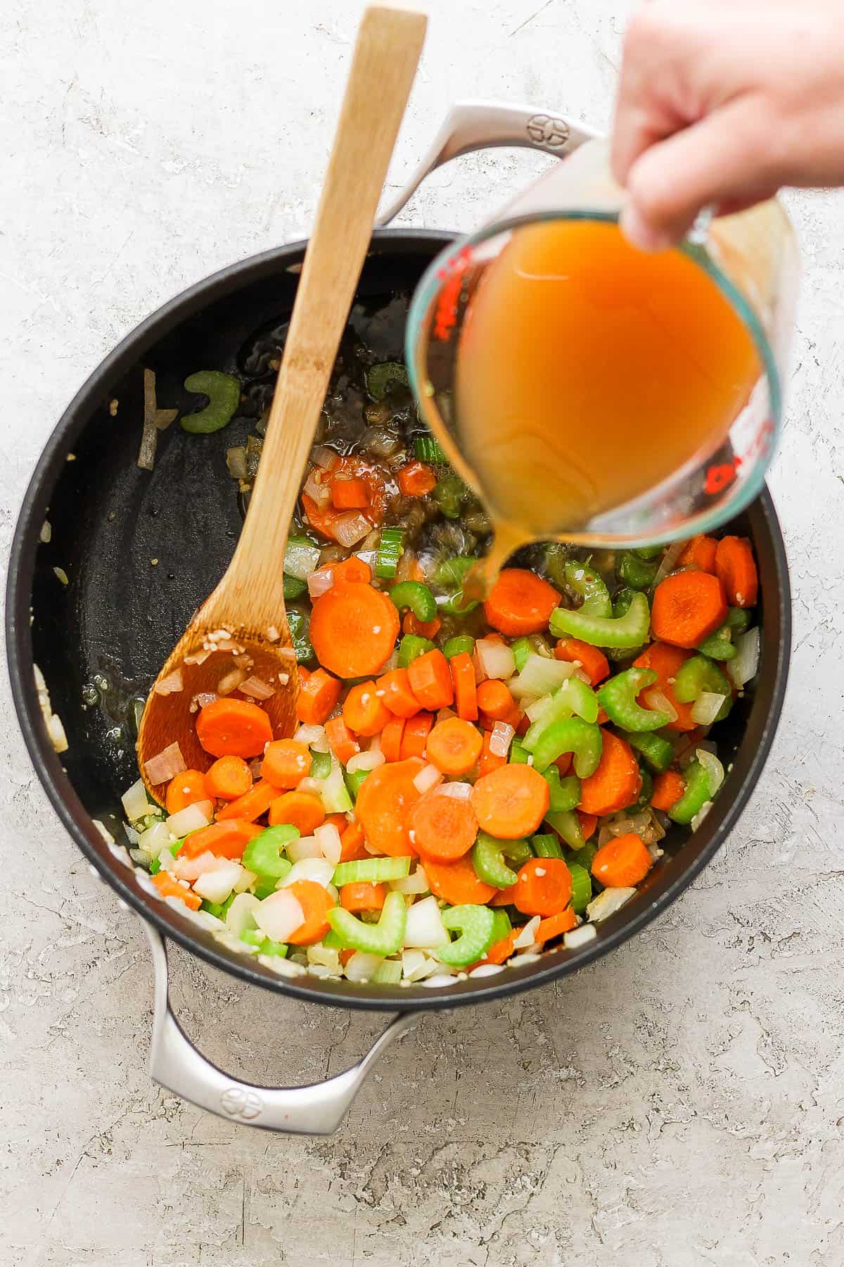 Chicken broth being poured into the sautéed vegetables.