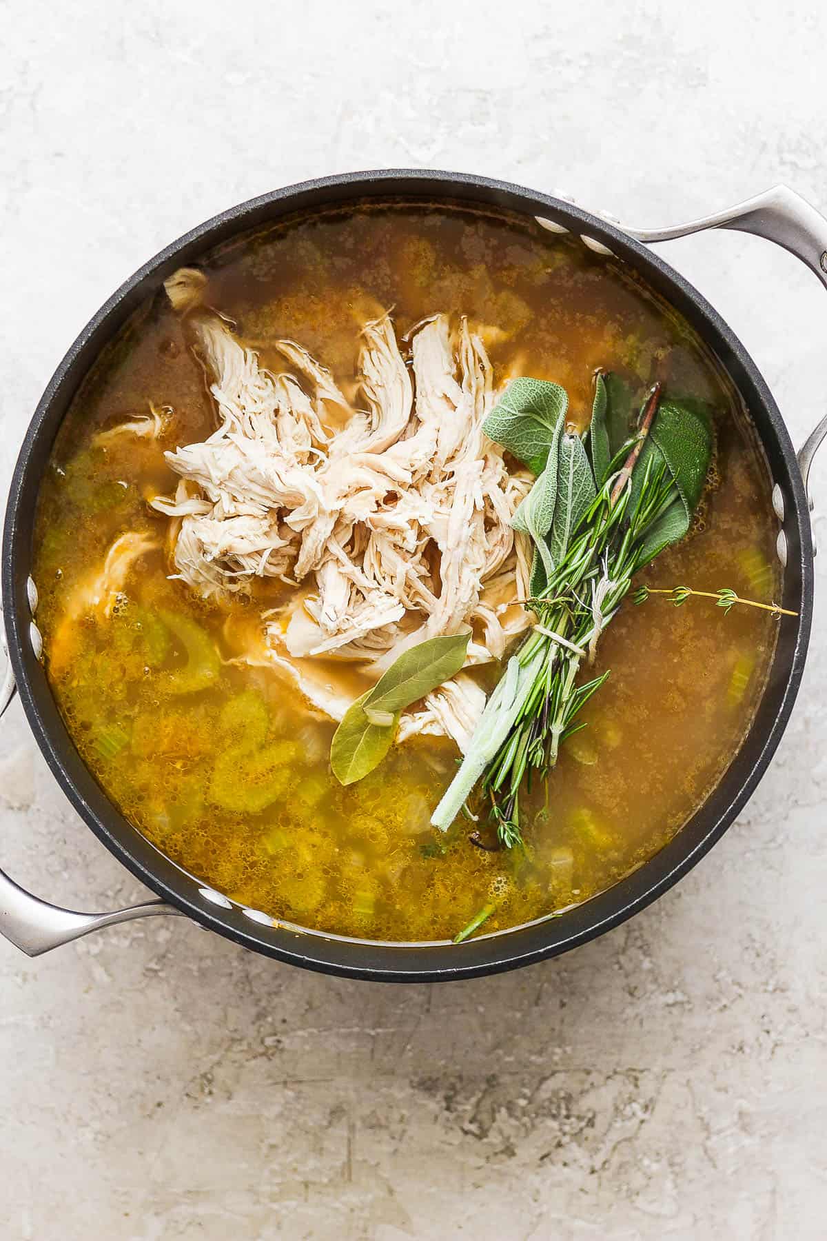 Shredded chicken added back to the broth and vegetables along with bay leaves, herb bundle, smashed garlic, and lemon zest.
