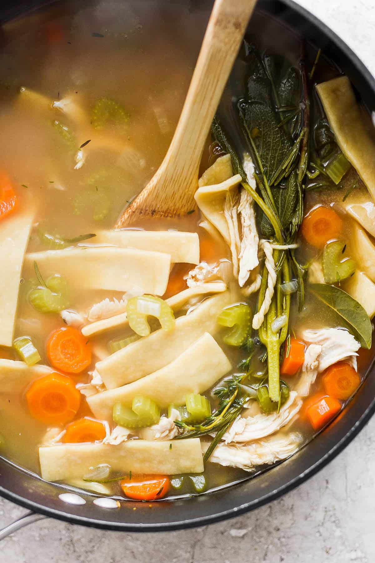A pot of homemade chicken noodle soup with a wooden spoon in it.