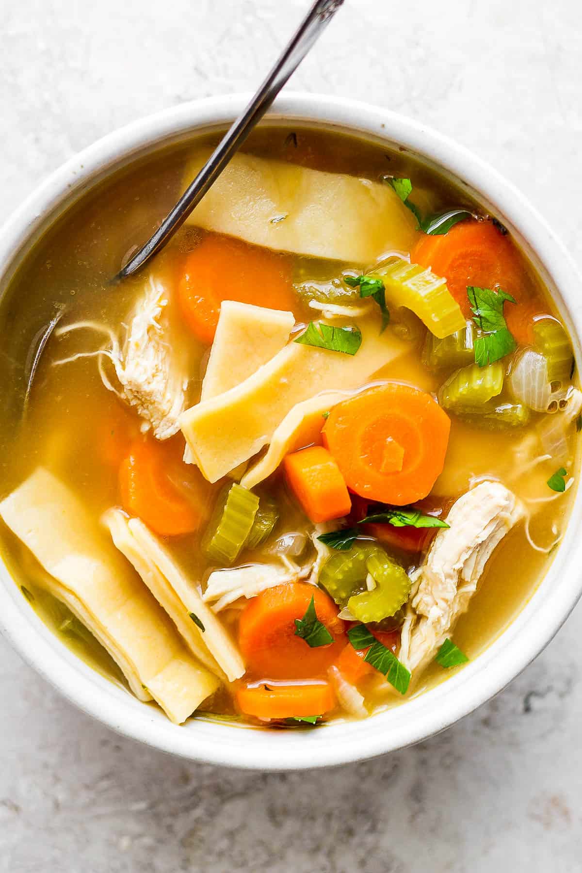 Chicken noodle soup in a white bowl with a spoon.