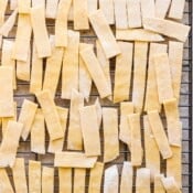 Top down shot of a wire rack filled with uncooked homemade noodles for soup on top all cut into 2 inch pieces.