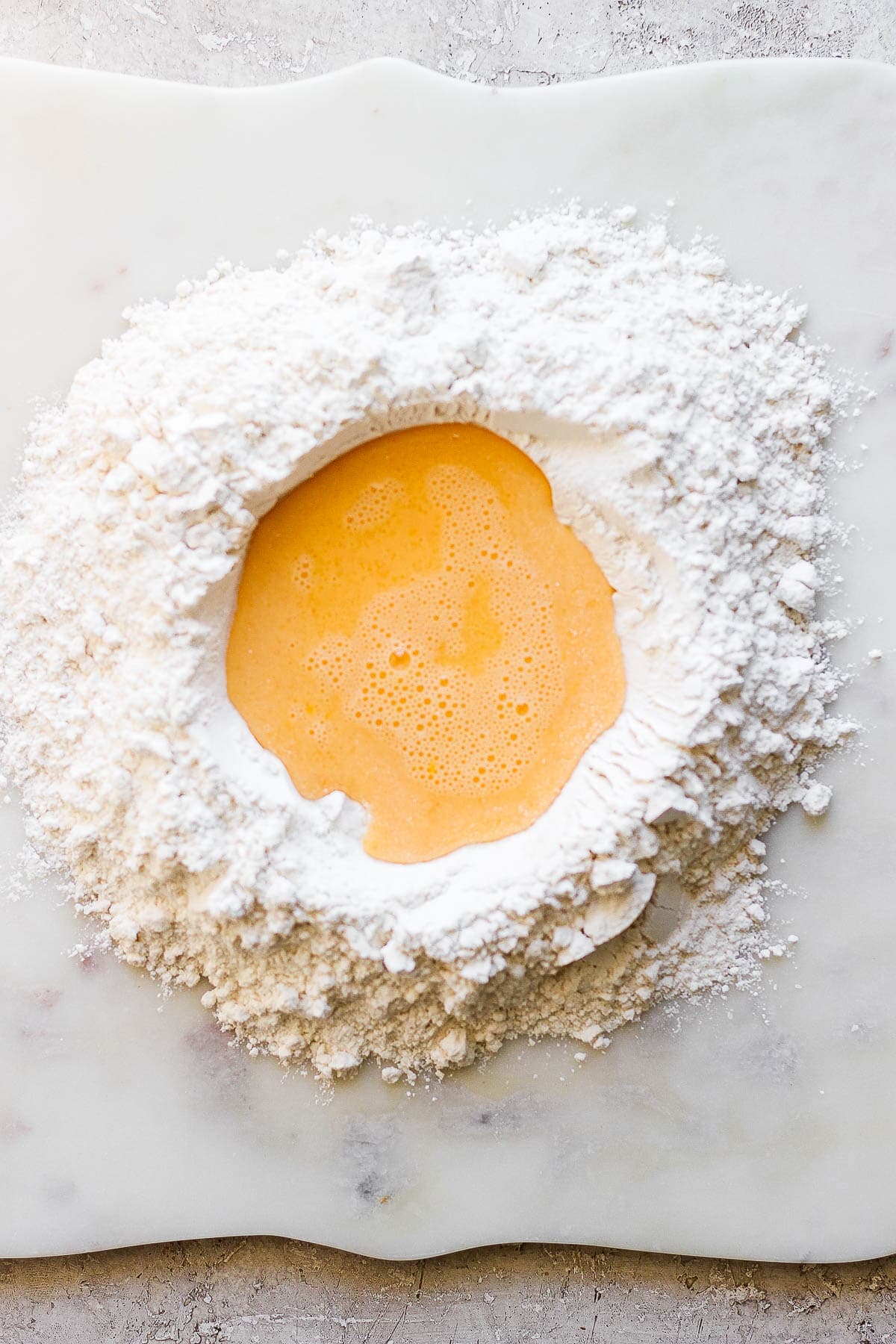 The flour and salt mixture is poured on a clean surface with the egg mixture poured in the middle.