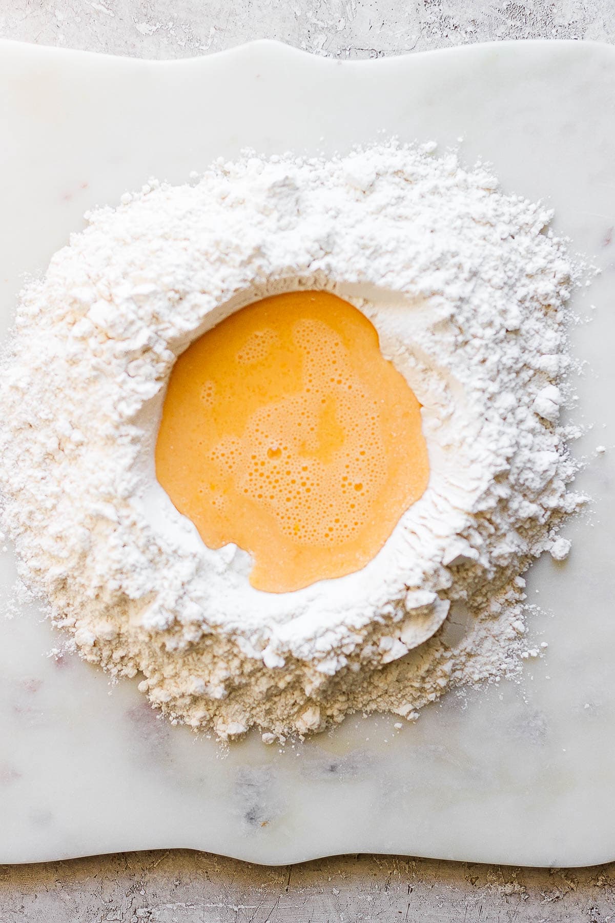 A well of flour on the counter with whisked eggs, water, and oil poured in the middle.