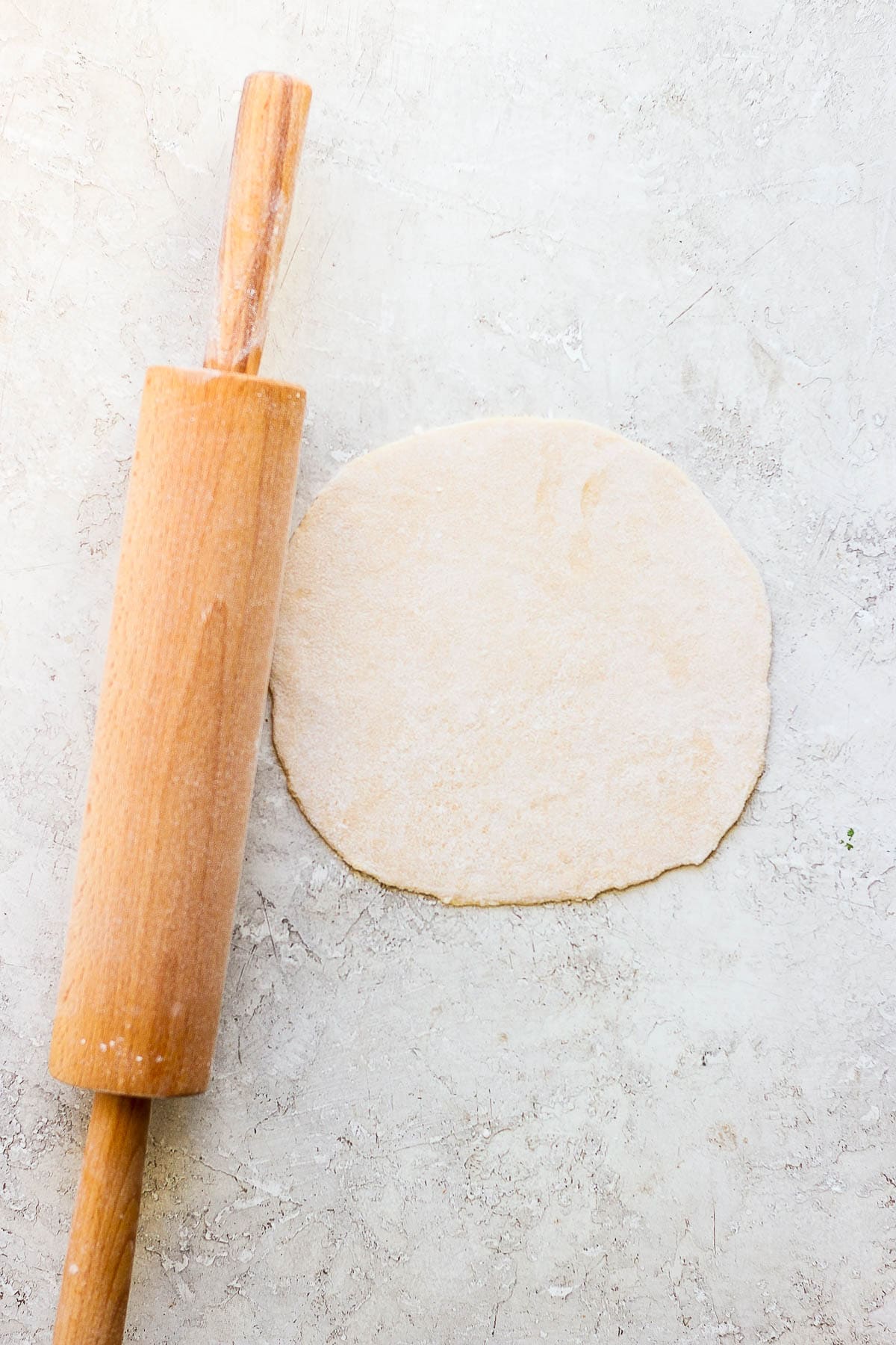 One of the dough parts rolled out thin and next to the rolling pin.