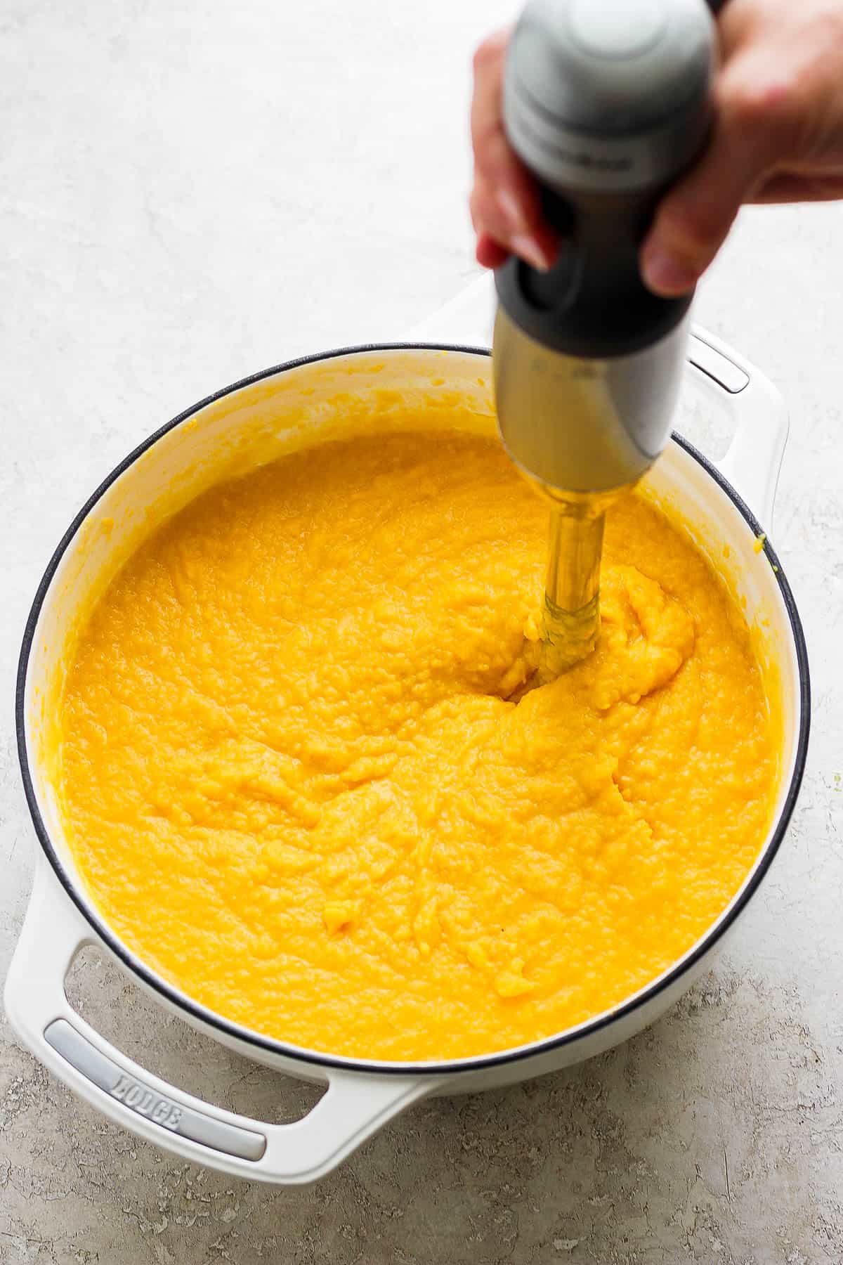 Pumpkin soup ingredients being blended by an immersion blender.