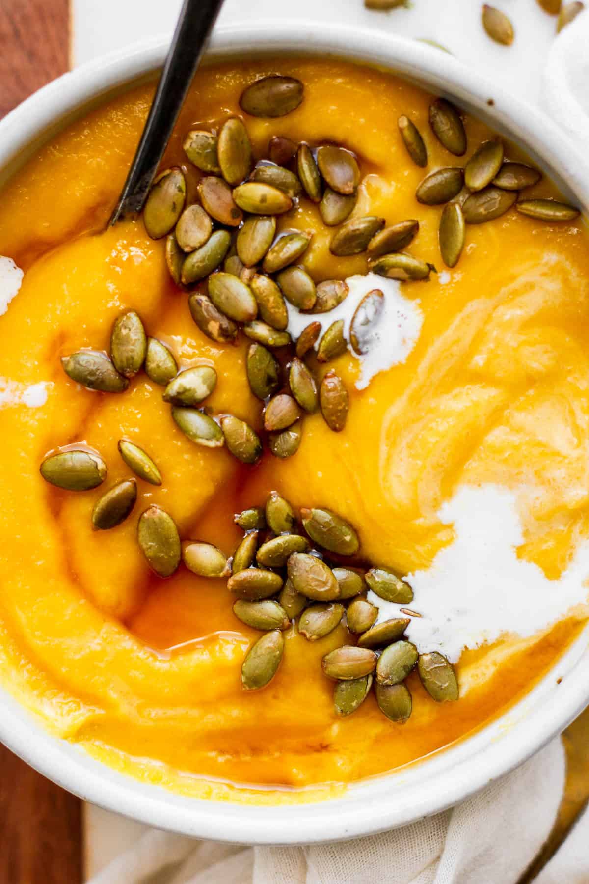 A cozy bowl of pumpkin soup with garnishes on top.